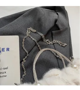 Detail of white faux fur handbag with rhinestone handle, pearl charm and silver chain strap