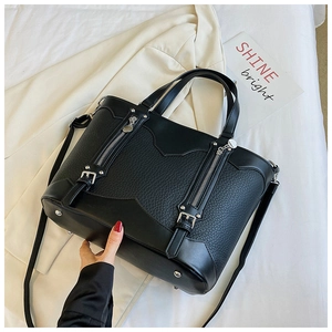 Detail of black pebbled leather tote bag featuring decorative zippers and metal buckles
