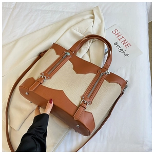 Detail of color-block tote bag with dual zippers, pebbled leather, and metal feet studs