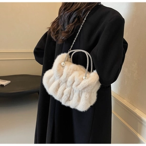 Detail of plush crossbody bag with rhinestone handle and metal chain on black coat