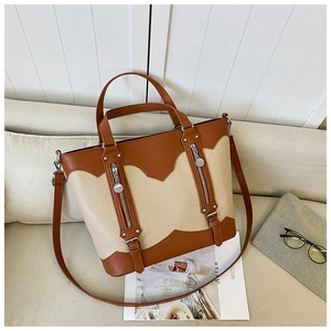 Detail view of two-tone leather tote bag with decorative zippers and hardware on a sofa