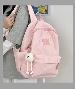 Detail of light pink backpack featuring vertical pleated texture and cute white plush ball