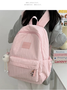 Detail of light pink pleated backpack featuring a branded logo and cute plush charms
