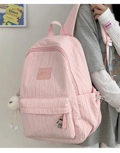 Detail view of pink pleated backpack showing vertical textures and fluffy ball keychain