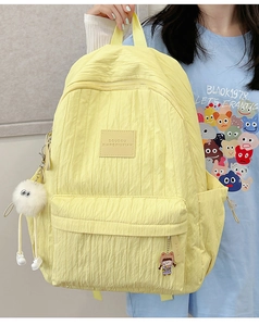 Close-up of pale yellow pleated backpack with soft texture and cute plush accessories