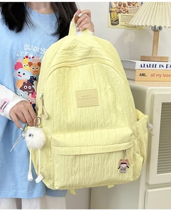 Detail view of a yellow pleated school backpack with plush pompom and cartoon pendants
