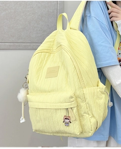 Detail of yellow school backpack showing vertical pleated texture and plush ball charm