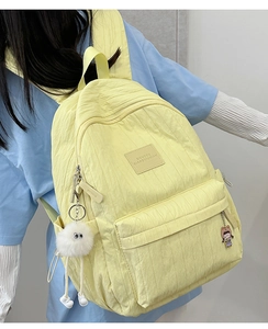 Side view of a yellow quilted backpack with cute plush charms on a model's back