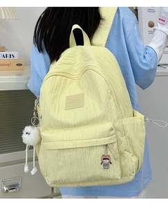 Detail of light yellow quilted backpack featuring side pockets and cute cartoon charms