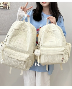 Detail showing two white bubble-textured backpacks in large and small sizes with charms
