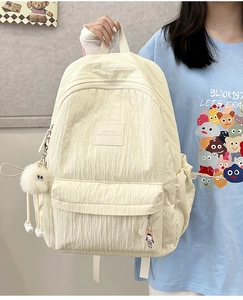 Detail of cream pleated backpack featuring multi-pocket design and cute plush charms