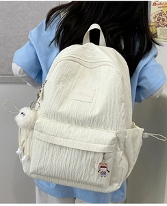 Off-white pleated backpack with plush charm shown from a 45-degree back view angle