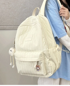 Detail of white bubble textured backpack featuring plush ball charm and side drawstring pockets