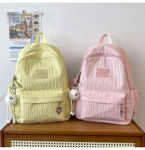 Detail of macaron yellow and pink school backpacks with pleated texture and cute charms