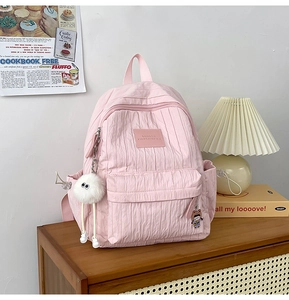 Pink pleated backpack with white plush charm on a wooden shelf in a cozy setting