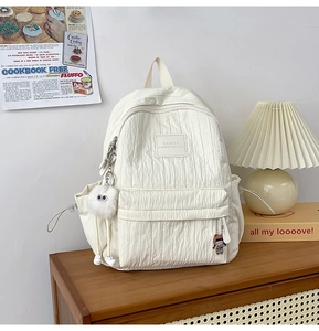 Detail of white bubble texture backpack with plush charm and brand tag on a wooden shelf
