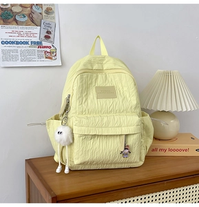 Detail of light yellow textured backpack with stylish charms and front zipper pocket
