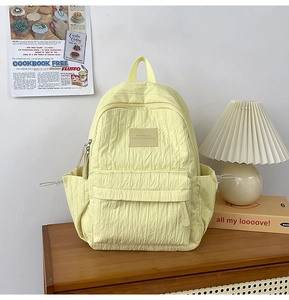 Detail of light yellow backpack showing soft vertical pleated texture and side drawstring pocket