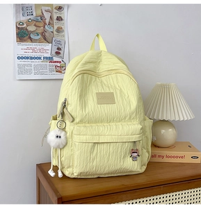 Detail of light yellow textured backpack with plush charm on a wooden cabinet