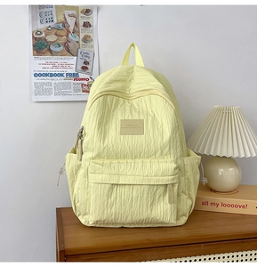 Detail of light yellow backpack with vertical pleats and leather brand label on a wooden desk