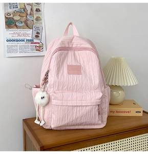 Pink bubble texture backpack with plush charm detail on a wooden cabinet shelf