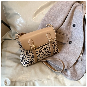 Detail of crossbody bag with leopard print canvas and khaki leather trim next to a grey blazer