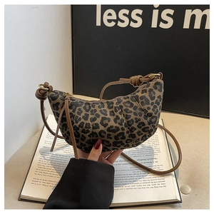 Detailed view of leopard print crescent bag with brown leather strap on an open book