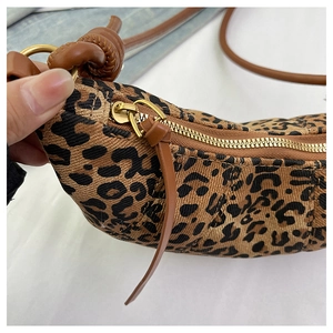 Detail of leopard print crossbody bag featuring bronze zipper and brown braided knot strap