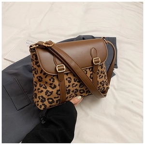 Close-up of leopard print crossbody bag with brown leather flap on white fabric