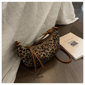 Close-up of leopard print crescent bag with leather strap and knot detail on wood floor