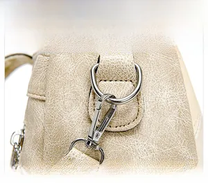 Macro shot of silver metal lobster clasp and D-ring on beige textured leather bag