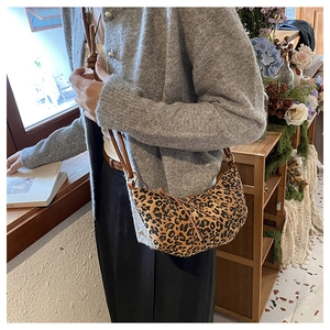 Detail of leopard print crescent bag with leather strap worn by a model in soft lighting