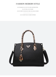 Detail of black pebbled leather handbag with leopard print handles and metal logo