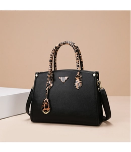 Detail of black pebbled leather handbag with leopard print handle and gold metal triangle