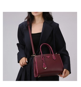 Detail of burgundy textured tote bag with triangular metal logo and adjustable strap