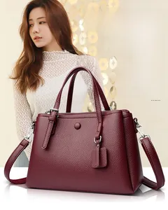 Macro shot of burgundy lychee leather texture and metallic strap hardware on a tote bag