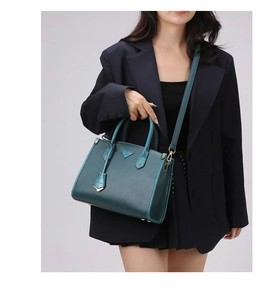 Detail of teal leather handbag with crocodile pattern handles and metal triangle badge