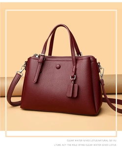Detailed view of burgundy lychee pattern leather handbag with handles and shoulder strap