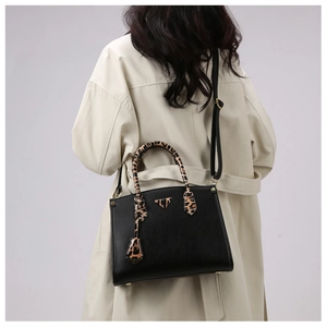 Detail of black leather handbag with leopard print handles and metal triangle plaque