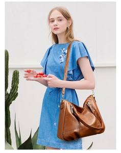 Detail of a large brown leather tote bag with adjustable strap on a blue denim dress