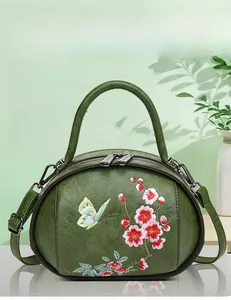 Detail of olive green handbag featuring floral embroidery and elegant metal zippers