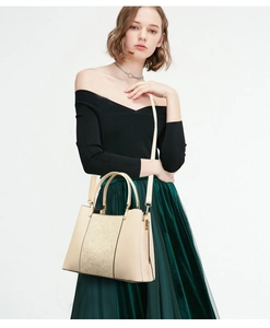 Close-up of beige embroidered tote bag with gold hardware held by an elegant model