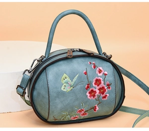 Close-up of vintage grey-blue handbag with floral embroidery and dual-zipper closure