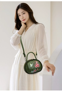 Detailed close-up of butterfly and pink flower embroidery on vintage green handbag