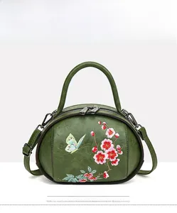 Macro detail of plum blossom and butterfly embroidery on a dark green vintage bag