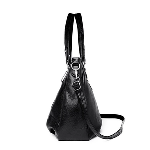 Minimalist black faux leather shoulder bag with top handles and adjustable strap on white background