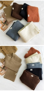 Close-up of ribbed knit scarves in various colors with fabric labels on a white surface