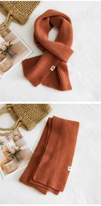 Close-up of thick burnt orange knit scarf with H-logo patch and soft texture detail