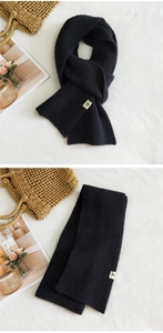 Detail of black ribbed knit scarf with a minimalist woven label on white linen