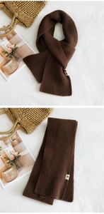 Detail of dark brown knit scarf showing thick ribbed texture and cute cat logo tag